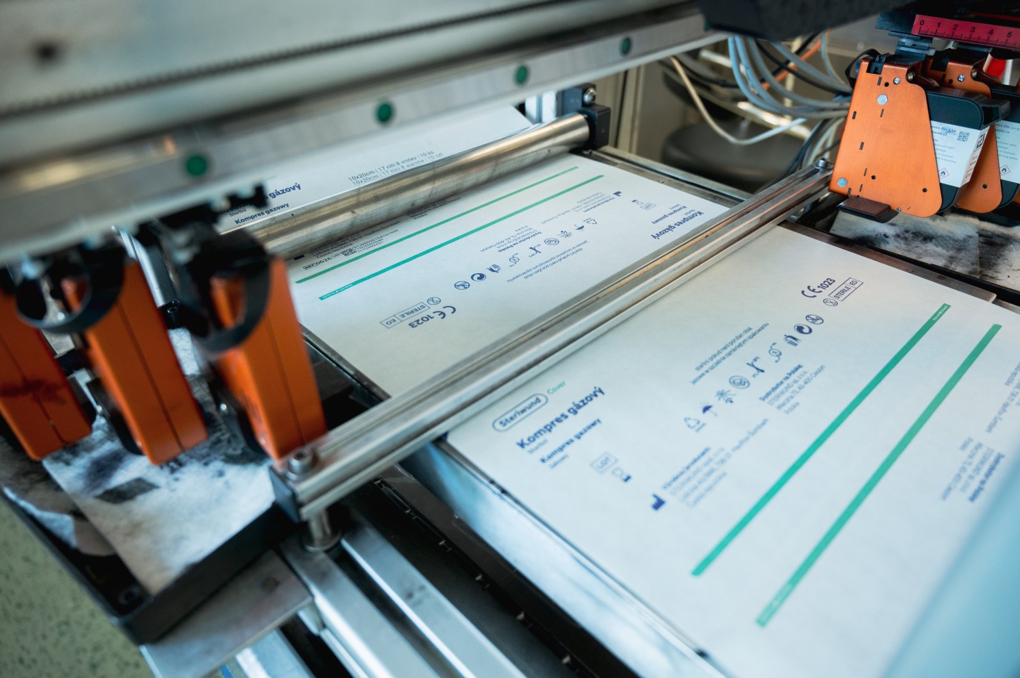 Tiskárna s HP cartridge (3x oranžová tiskárna) na pojezdu pro potisk Tyvek obalového materiálu ve zdravotnické výrobě. Kroková balící linka posune o dvě pozice obal a dva vozíky s tiskárnami pohybující se proti sobě značí současně dva produkty.